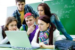 students surrounding laptop near blackboard