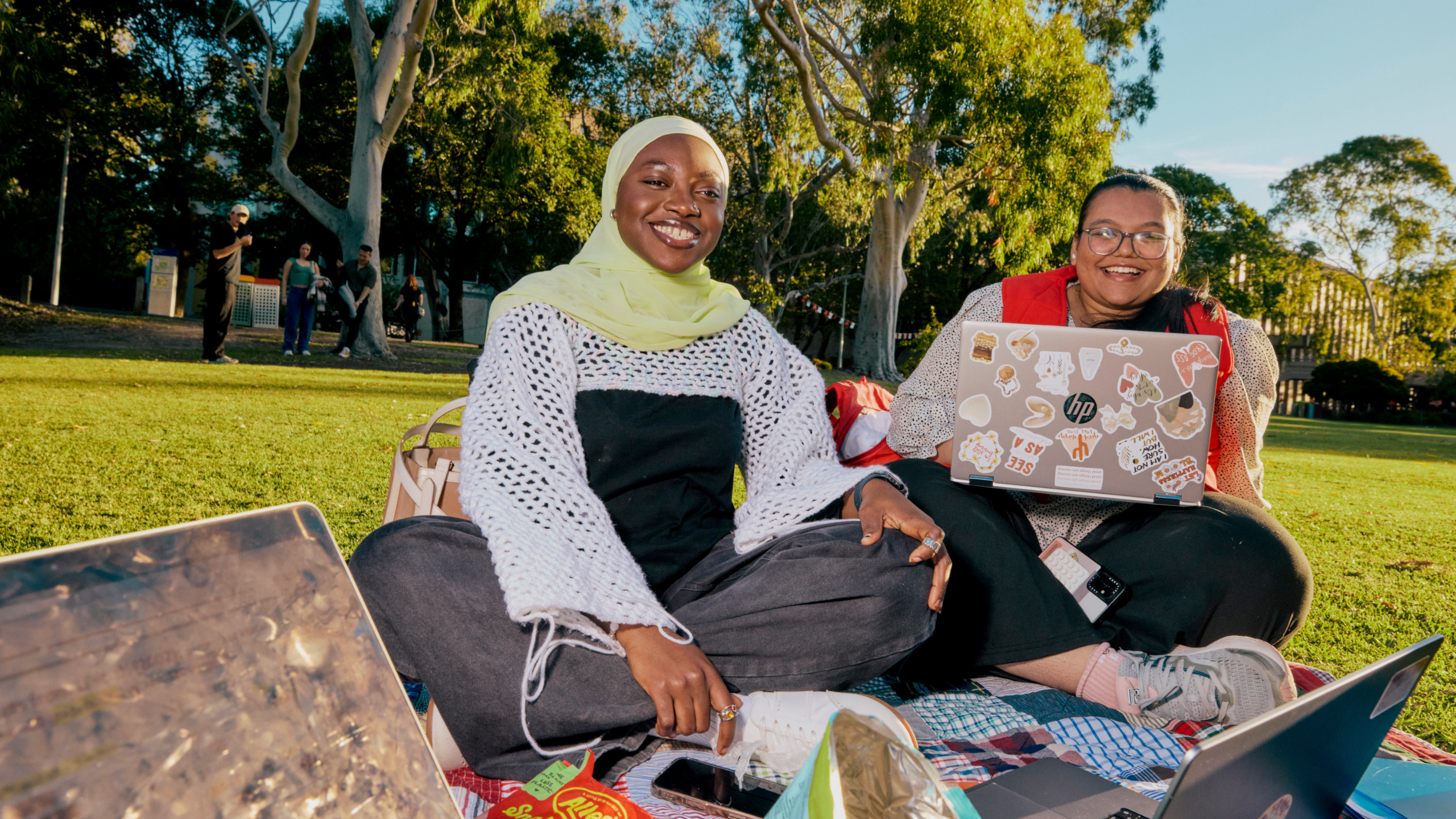 Two students sitting outside smiling with their laptop