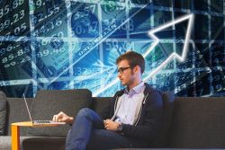 male sitting on couch looking at laptop with virtual background of blue colours with equations written in white