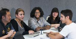 students sitting around table with laptops and notepads, talking and working collaboratively 